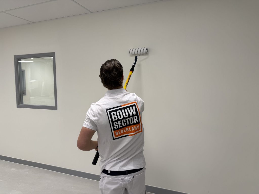 Schilder rolt met een gele verlengsteel een witte wand in een lege ruimte