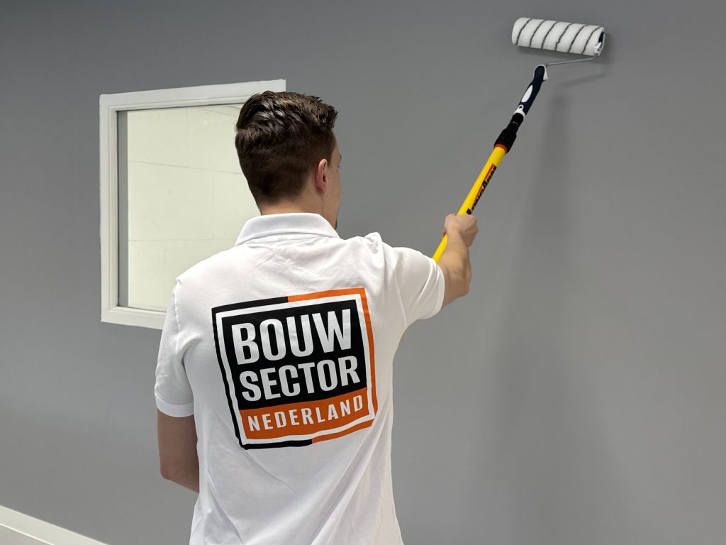 Schilder van Bouwsector Nederland rolt grijze muurverf op een wand naast een raam