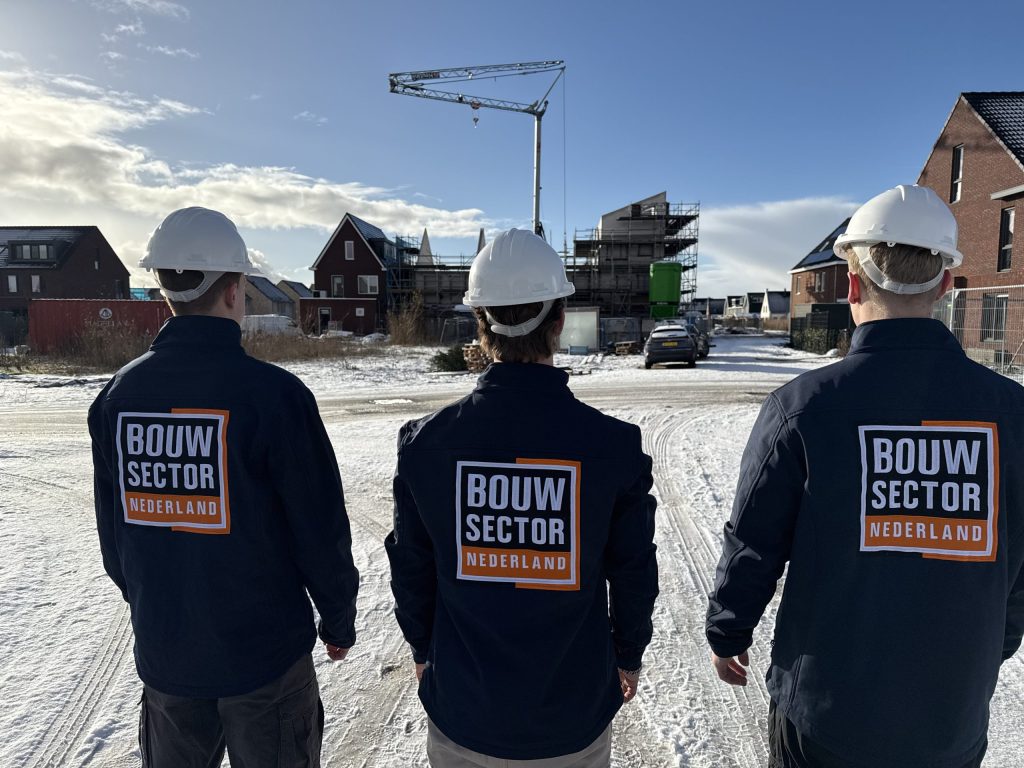 Drie vakmensen van Bouwsector Nederland met witte helm voor een rij woningen